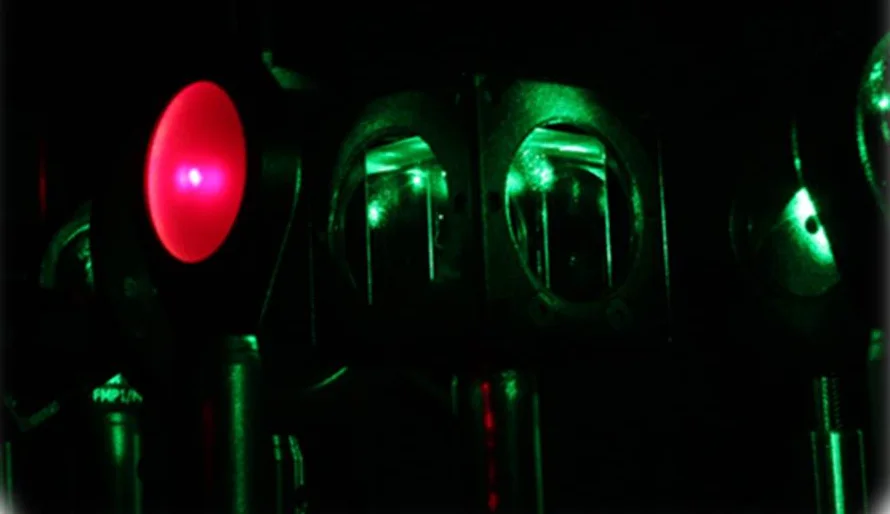 Abstract optical setup with red and green lights representing quantum entanglement in a dark laboratory.